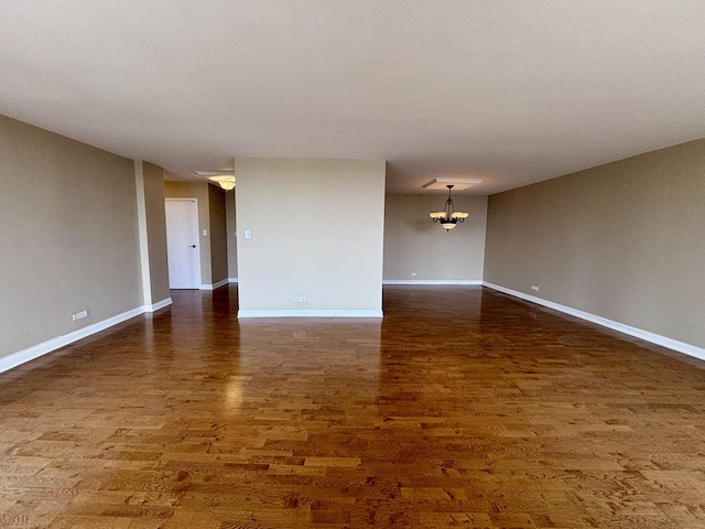 spare room featuring baseboards, an inviting chandelier, and dark wood finished floors