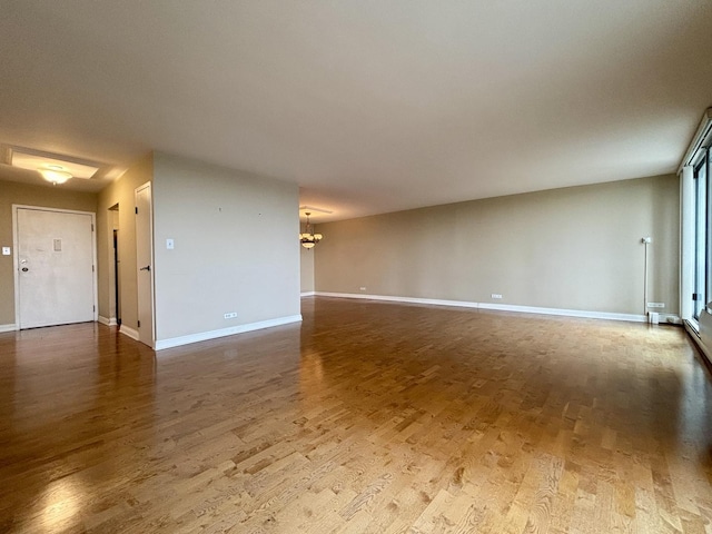 unfurnished room featuring baseboards, a chandelier, and wood finished floors