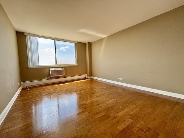 spare room featuring wood finished floors, baseboards, a wall unit AC, and a baseboard heating unit