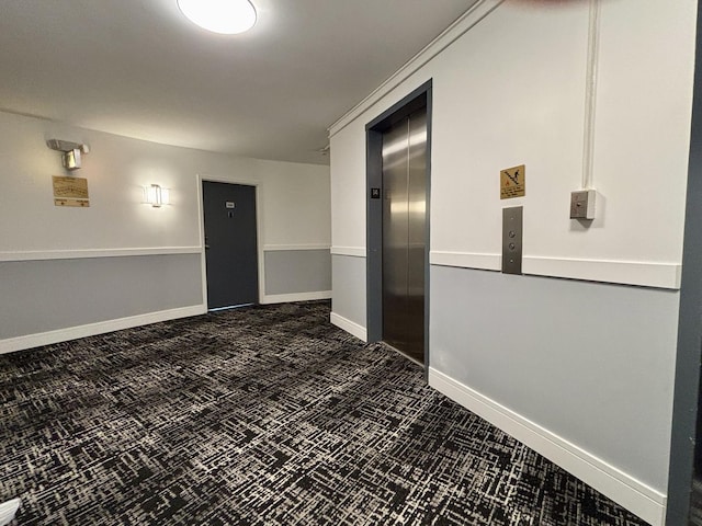 unfurnished room featuring baseboards, dark colored carpet, and elevator