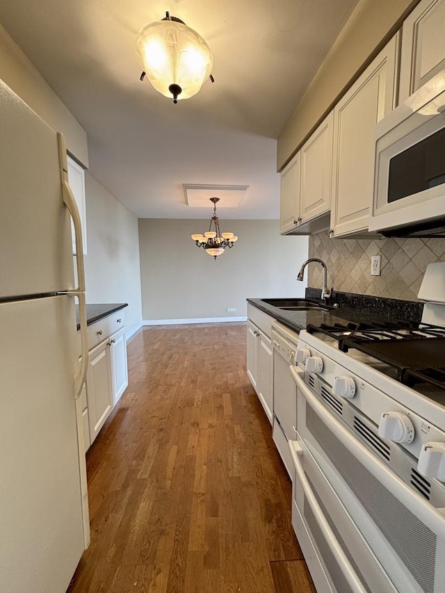 kitchen featuring decorative backsplash, dark countertops, a sink, white cabinets, and white appliances