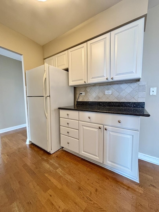 kitchen featuring decorative backsplash, white cabinets, freestanding refrigerator, and wood finished floors
