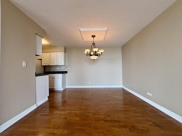 unfurnished dining area with baseboards, dark wood finished floors, and a chandelier
