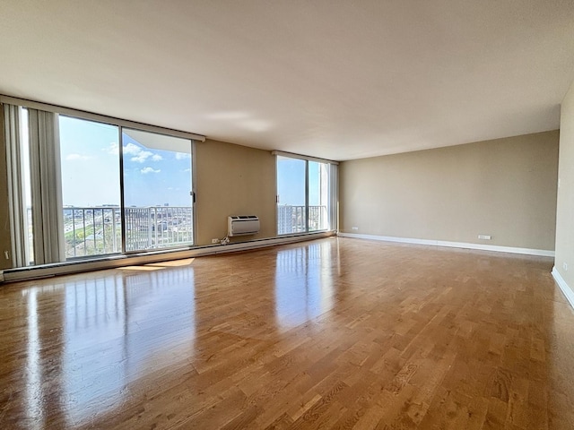 empty room featuring baseboards, floor to ceiling windows, a wall mounted air conditioner, and wood finished floors