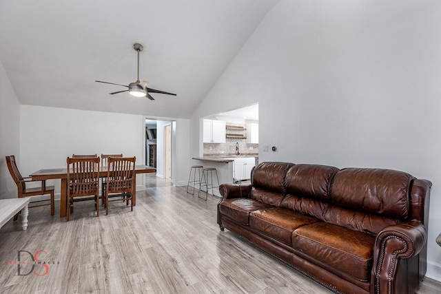 living room with a ceiling fan, high vaulted ceiling, light wood-style flooring, and baseboards