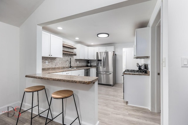 kitchen featuring tasteful backsplash, appliances with stainless steel finishes, a breakfast bar area, a peninsula, and light wood-style floors