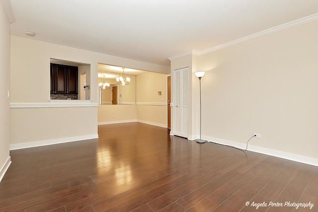 empty room featuring dark wood-style floors, ornamental molding, baseboards, and a notable chandelier