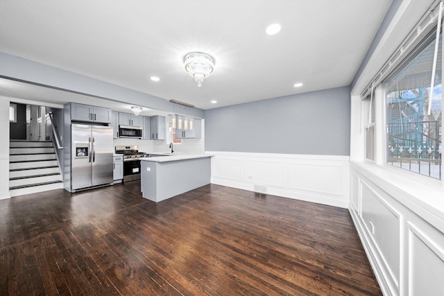 kitchen with stainless steel appliances, gray cabinets, light countertops, wainscoting, and a peninsula