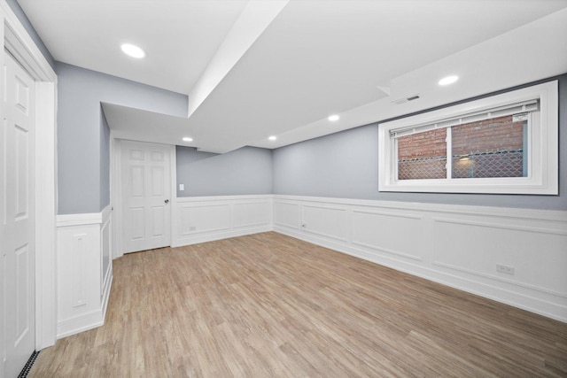 finished below grade area featuring wainscoting, light wood-style flooring, visible vents, and recessed lighting