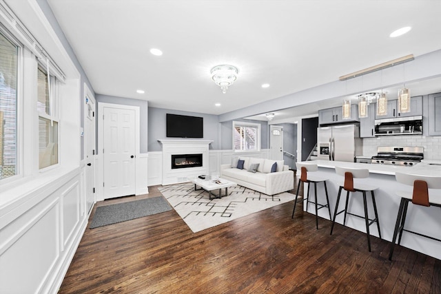 living room with a decorative wall, recessed lighting, dark wood-type flooring, wainscoting, and a glass covered fireplace