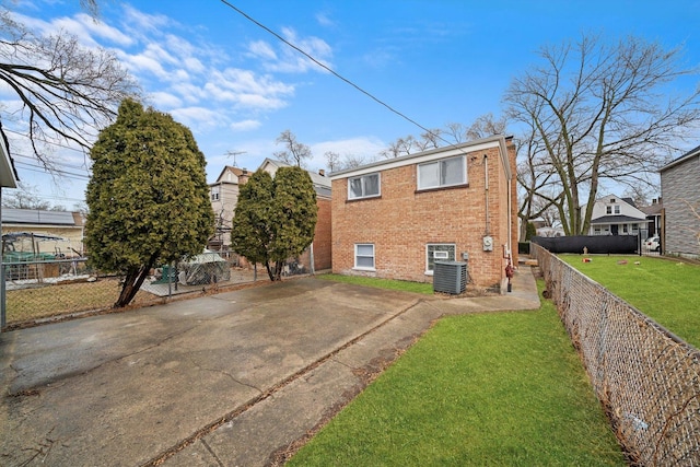 rear view of property featuring fence private yard, brick siding, central AC, and a yard