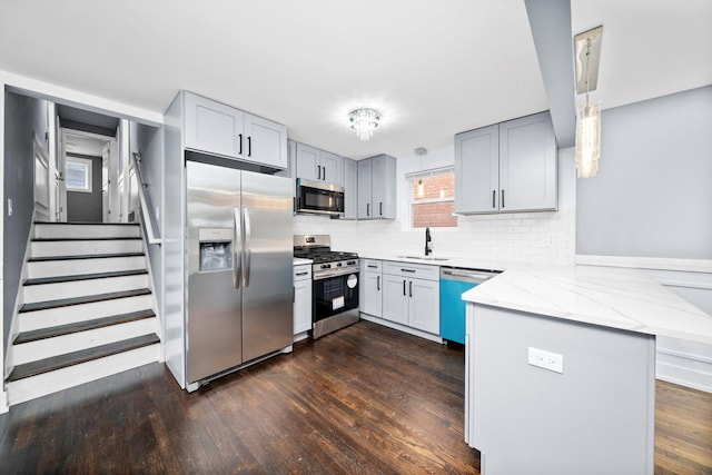 kitchen featuring dark wood-style floors, a peninsula, light stone countertops, stainless steel appliances, and a sink