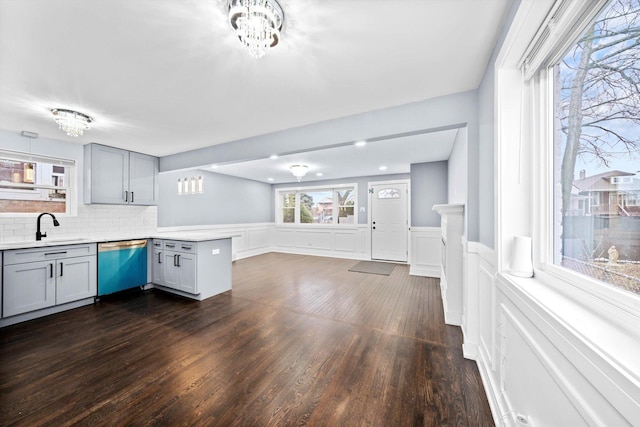 kitchen featuring dishwashing machine, a peninsula, a sink, light countertops, and gray cabinets