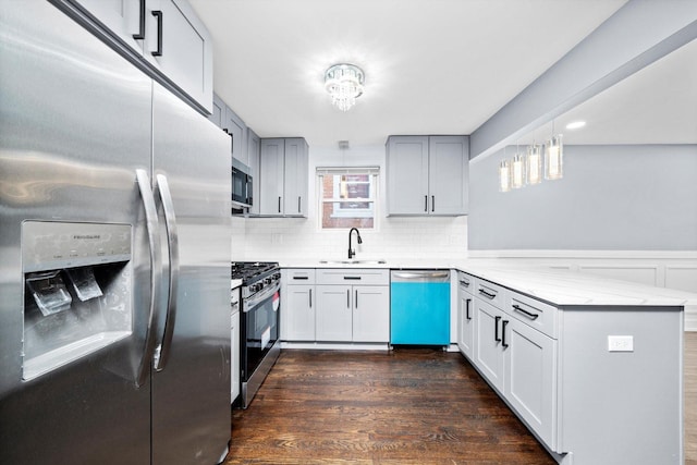 kitchen with light stone counters, stainless steel appliances, dark wood-type flooring, a peninsula, and a sink