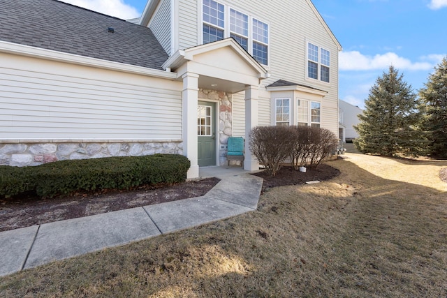 property entrance featuring a yard, stone siding, and roof with shingles