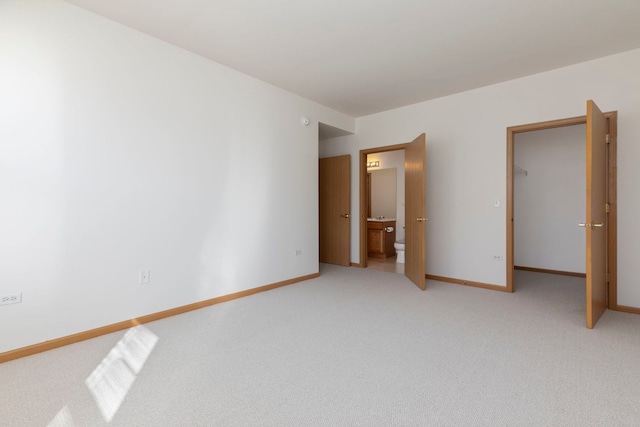 unfurnished bedroom featuring connected bathroom, baseboards, and light carpet