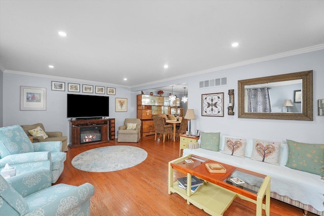 living area with crown molding, recessed lighting, visible vents, a glass covered fireplace, and wood finished floors