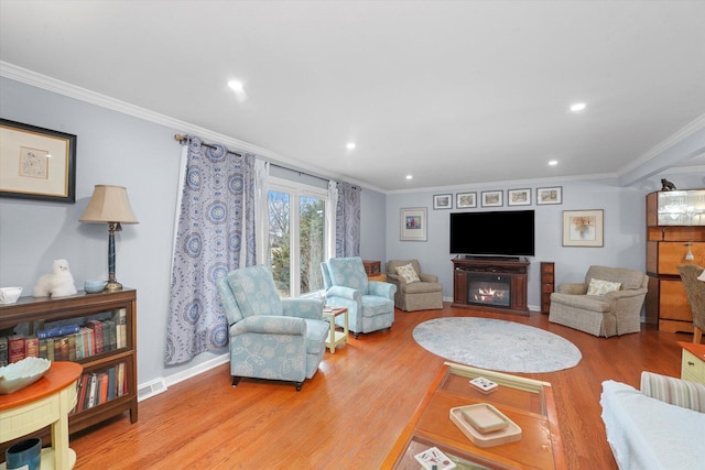 living area with visible vents, a glass covered fireplace, wood finished floors, and ornamental molding