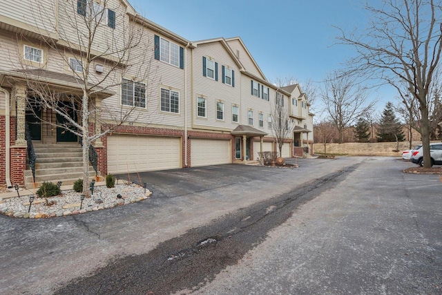 exterior space with a garage, driveway, brick siding, and a residential view