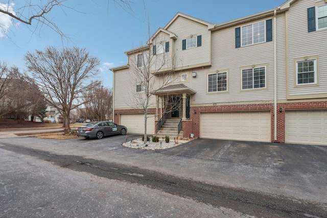 view of property featuring aphalt driveway, brick siding, and an attached garage