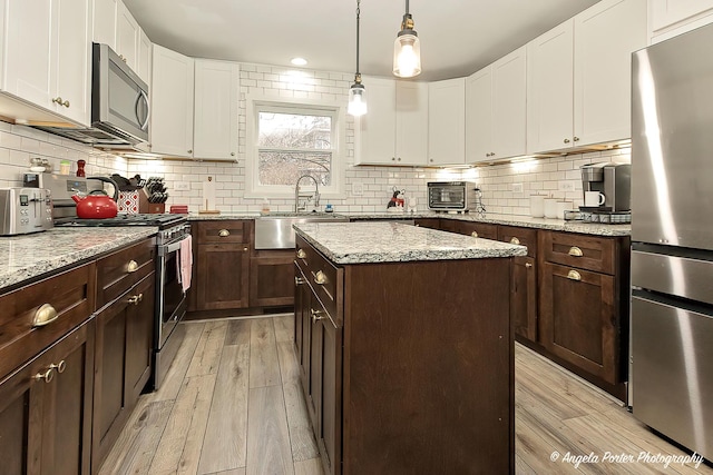 kitchen with appliances with stainless steel finishes, light wood-type flooring, white cabinetry, and a sink