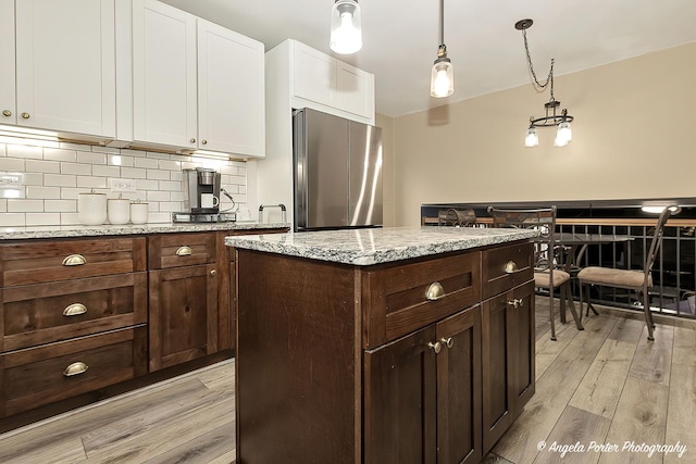 kitchen featuring light wood finished floors, white cabinets, decorative backsplash, freestanding refrigerator, and pendant lighting