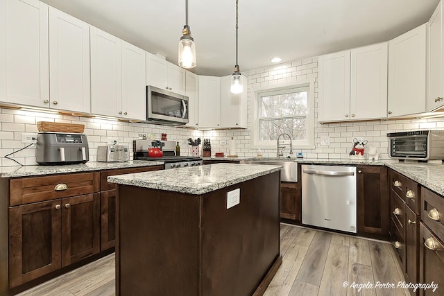 kitchen with appliances with stainless steel finishes, light wood-type flooring, white cabinetry, and tasteful backsplash