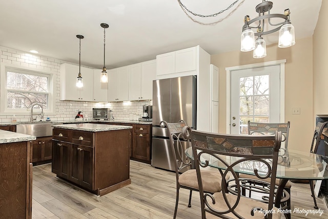 kitchen with dark brown cabinetry, a sink, backsplash, freestanding refrigerator, and a center island