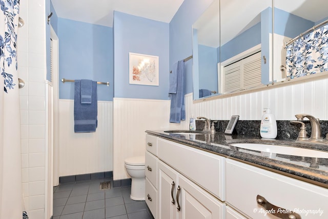 bathroom featuring a wainscoted wall, a sink, toilet, and tile patterned floors