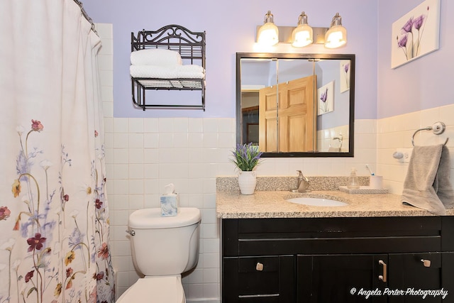 bathroom featuring toilet, a shower with shower curtain, vanity, tile walls, and wainscoting