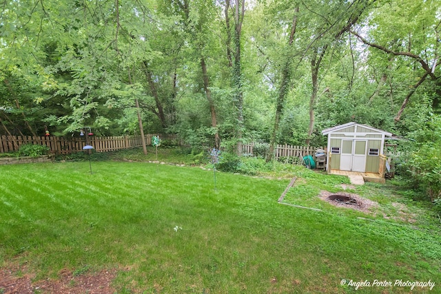 view of yard featuring an outbuilding, a fenced backyard, a wooded view, and a storage unit