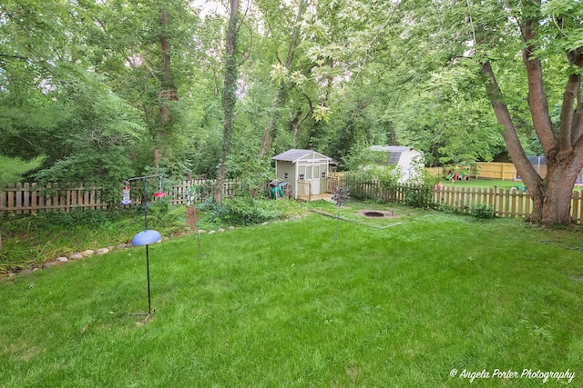 view of yard featuring a wooded view, a fenced backyard, an outdoor structure, and a storage shed