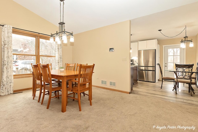 dining room featuring lofted ceiling, light colored carpet, visible vents, and an inviting chandelier