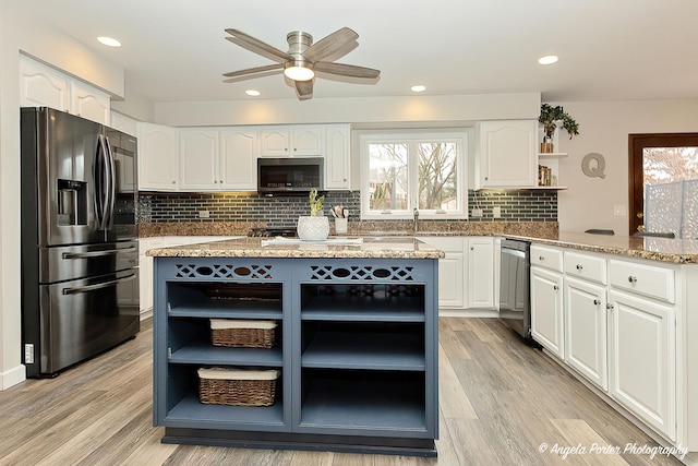 kitchen featuring appliances with stainless steel finishes, light stone counters, white cabinetry, open shelves, and a wealth of natural light