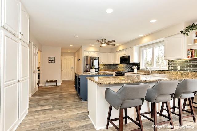 kitchen featuring stainless steel refrigerator with ice dispenser, light wood-style flooring, white cabinetry, black microwave, and a peninsula