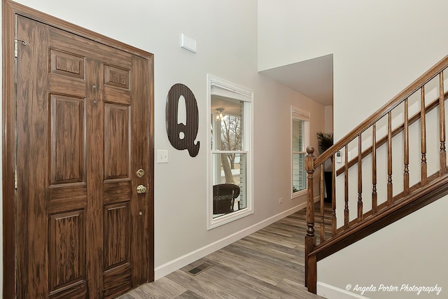 foyer featuring light wood finished floors, baseboards, visible vents, and stairway