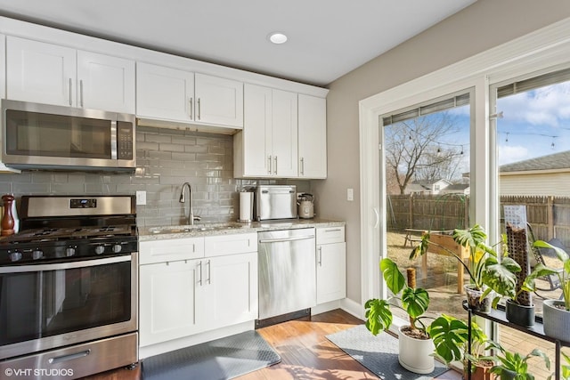 kitchen with backsplash, appliances with stainless steel finishes, wood finished floors, white cabinetry, and a sink