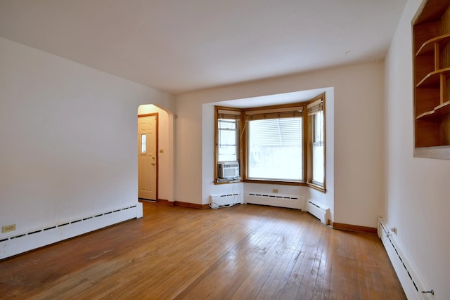 empty room featuring arched walkways, a baseboard radiator, hardwood / wood-style floors, a baseboard heating unit, and baseboards