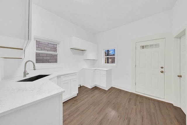 kitchen featuring light wood finished floors, baseboards, light stone countertops, white cabinetry, and a sink