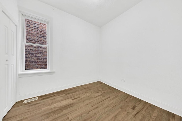 unfurnished room featuring wood finished floors, visible vents, and baseboards