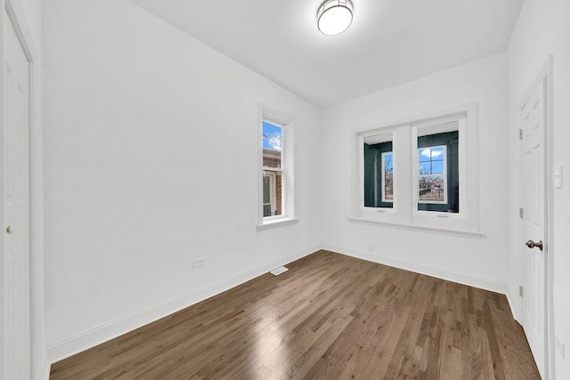 empty room with a healthy amount of sunlight, wood finished floors, and baseboards