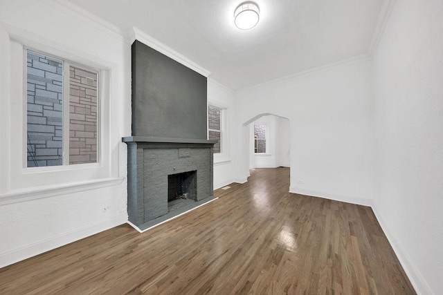 unfurnished living room featuring baseboards, arched walkways, ornamental molding, wood finished floors, and a fireplace