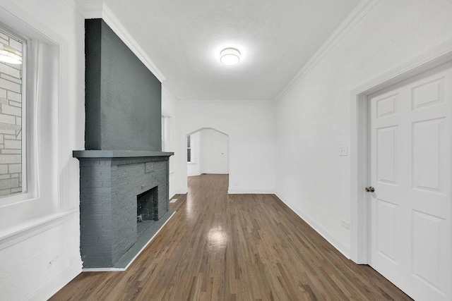 unfurnished living room featuring arched walkways, wood finished floors, baseboards, a brick fireplace, and crown molding