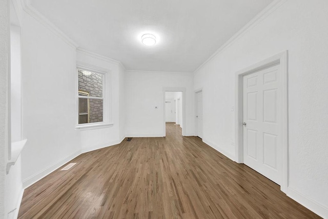 empty room with ornamental molding, wood finished floors, visible vents, and baseboards