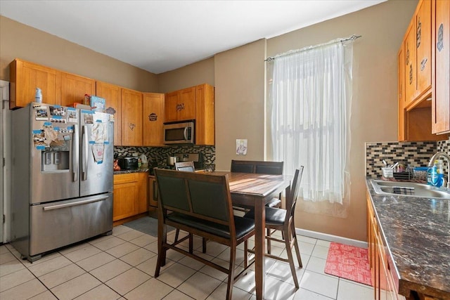 kitchen with brown cabinets, light tile patterned floors, stainless steel appliances, backsplash, and a sink