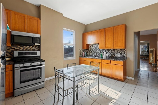 kitchen with stainless steel range with gas cooktop, light tile patterned floors, dark countertops, backsplash, and a sink