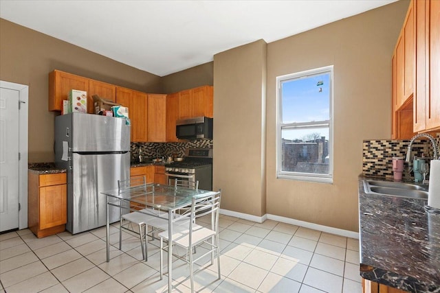 kitchen with baseboards, decorative backsplash, appliances with stainless steel finishes, a sink, and light tile patterned flooring