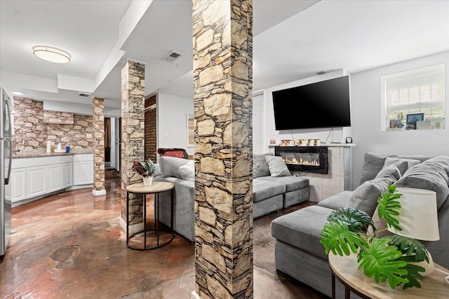 living area with a glass covered fireplace, visible vents, decorative columns, and finished concrete flooring