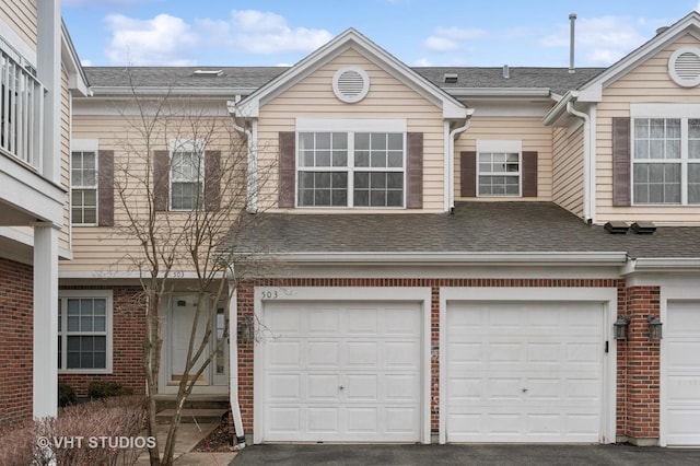 townhome / multi-family property featuring a garage, brick siding, driveway, and a shingled roof