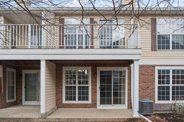 property entrance featuring a balcony, brick siding, and central AC